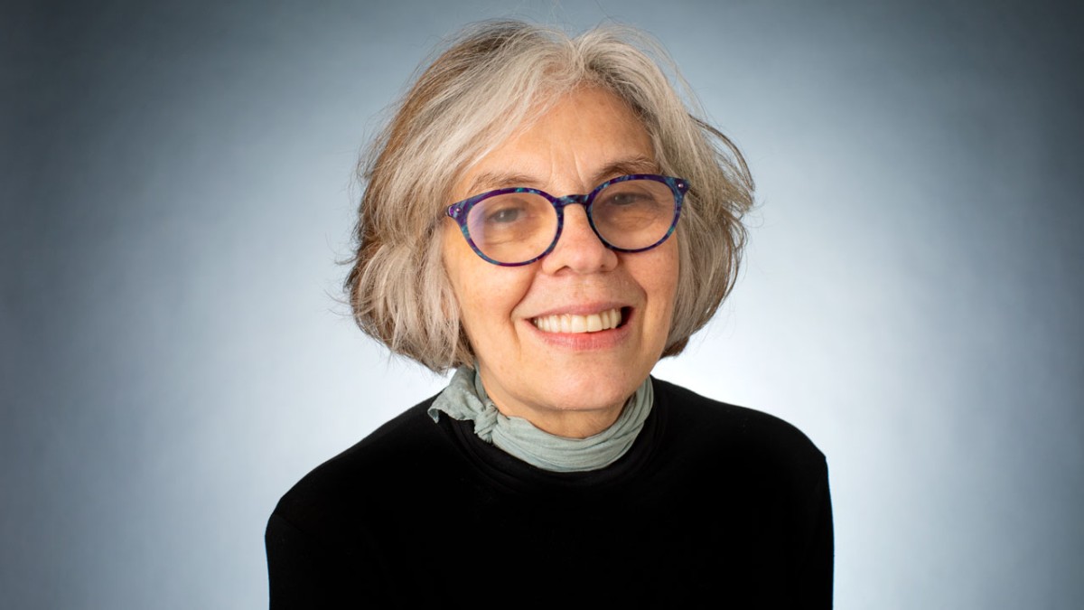 A photo of Carla Gomes, a woman with light brown - gray hair, glasses and a black sweater in front of a gray background