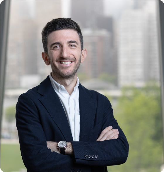 A color portrait of a man in front of a window showing NYC in the background.
