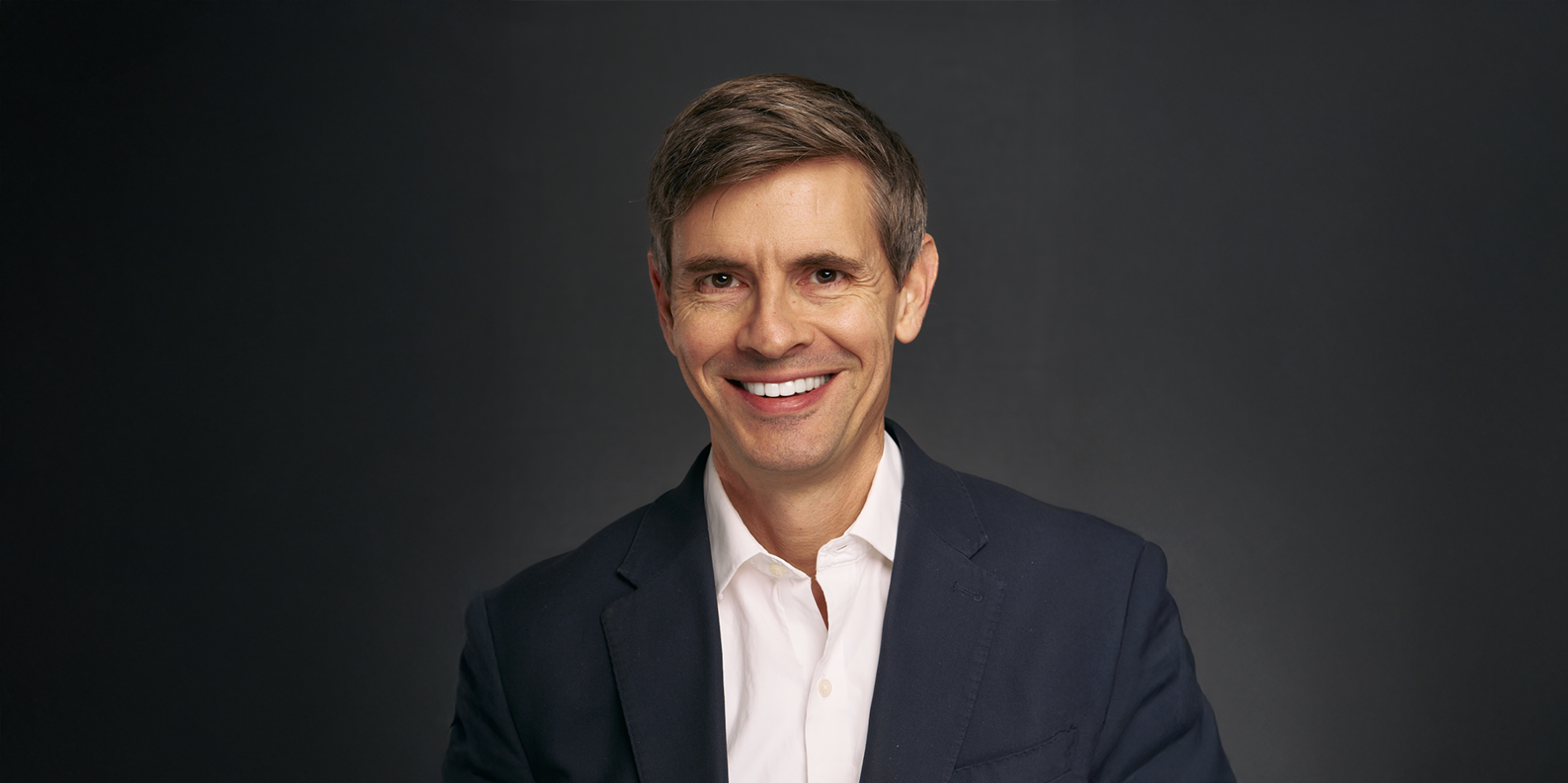 A color photo of a man smiling for a portrait.