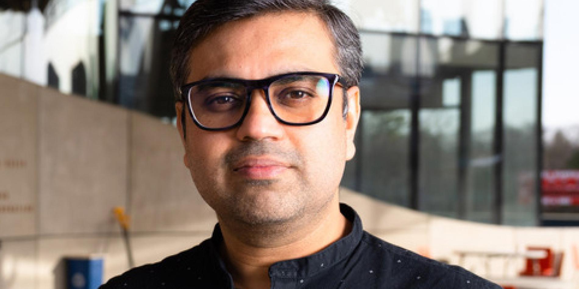  Aditya Vashistha stands and stares at the camera wearing a button-down shirt