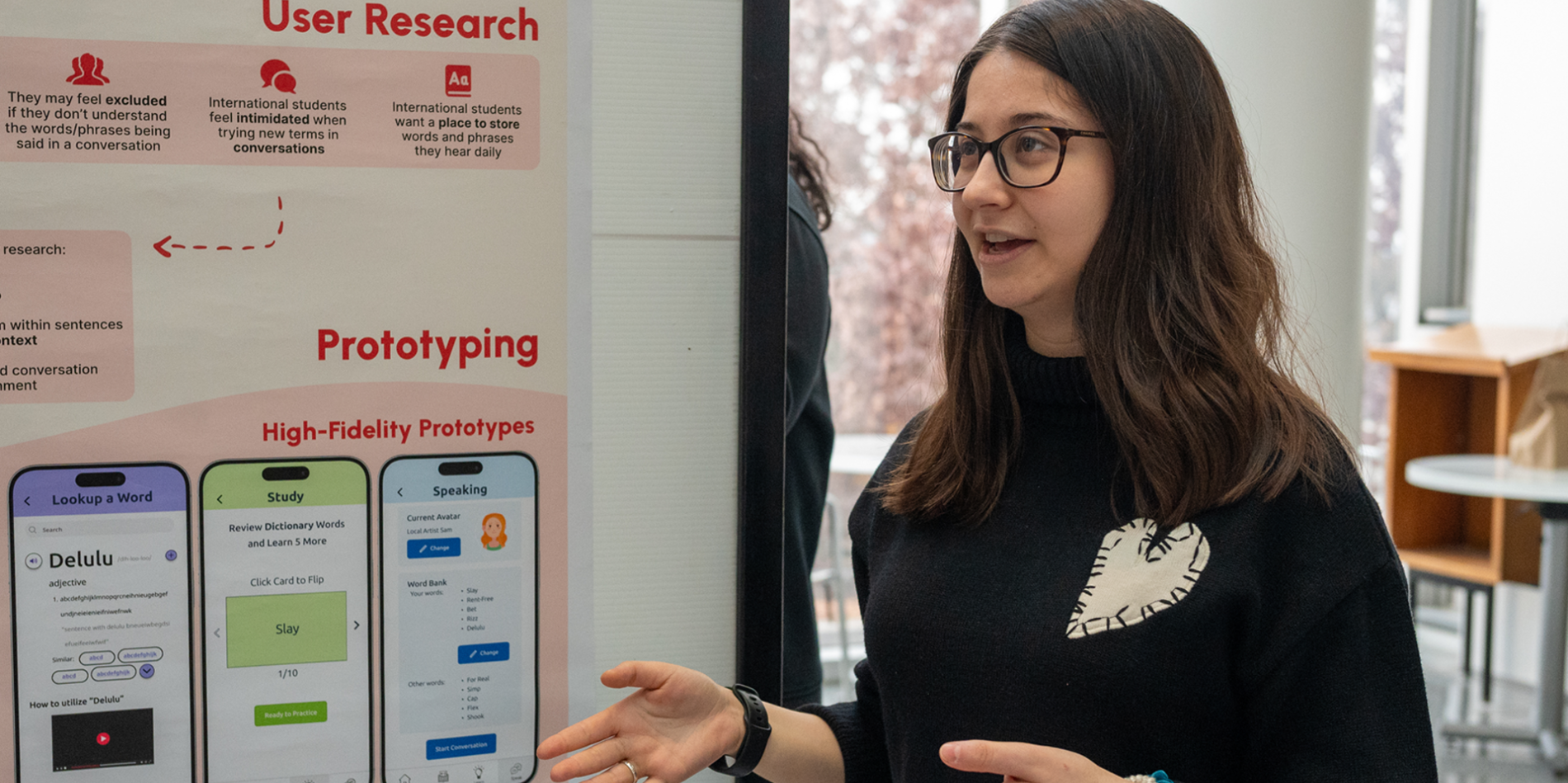 a female student with long brown hair and glasses presents in front of a poster
