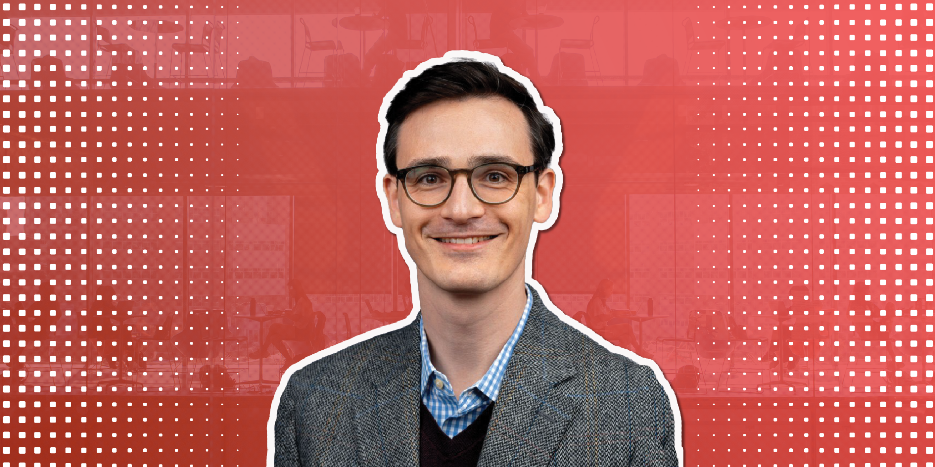 a man with brown hair and glasses smiles in front of a red background