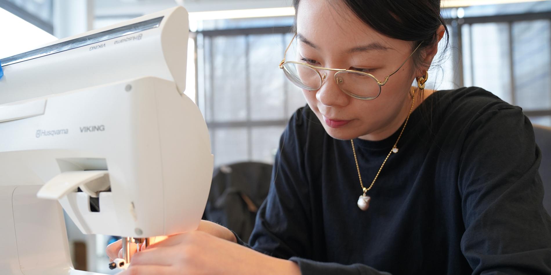 A woman in a black top sits and works on a sewing machine