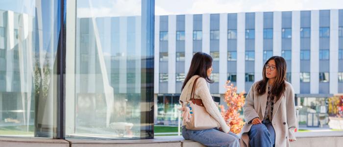 two students sit on ledge outside Gates Hall