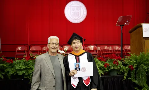 A color photo of a recent graduate in regalia with a family member.