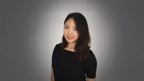 A color photo of woman in a black dress in front of a grey background.