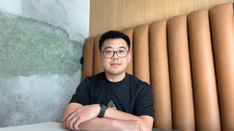A color photo of a man with glasses sitting in a restaurant booth.