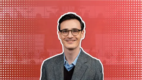 a man with brown hair and glasses smiles in front of a red background