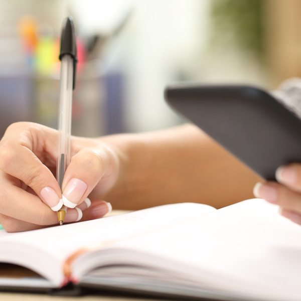 A color photo showing a person using a smart phone and writing down notes. Shutterstock