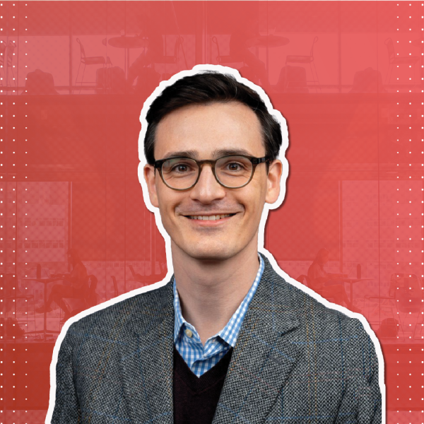 a man with brown hair and glasses smiles in front of a red background