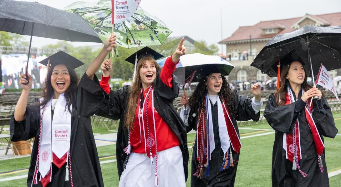 a group of female graduates in caps and gowns point and wave on the field during commencement