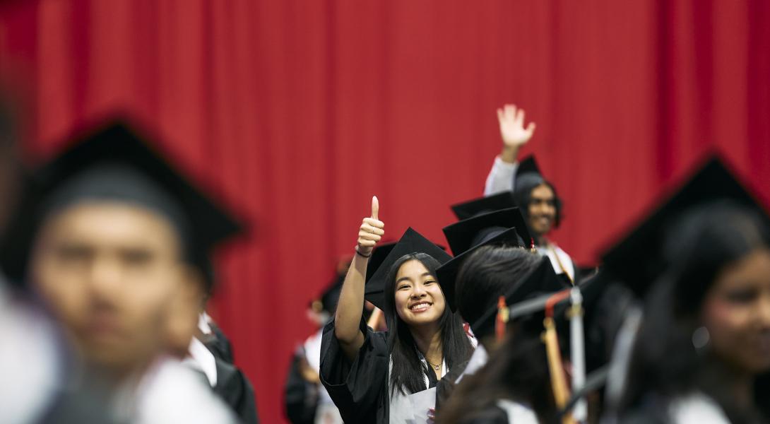 a female graduate gives a thumbs up in the crowd