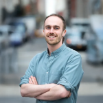 A color photo of a man standing with his arms crossed.