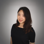 A color photo of woman in a black dress in front of a grey background.