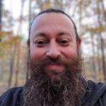 a man with a long brown beard smiling in the woods