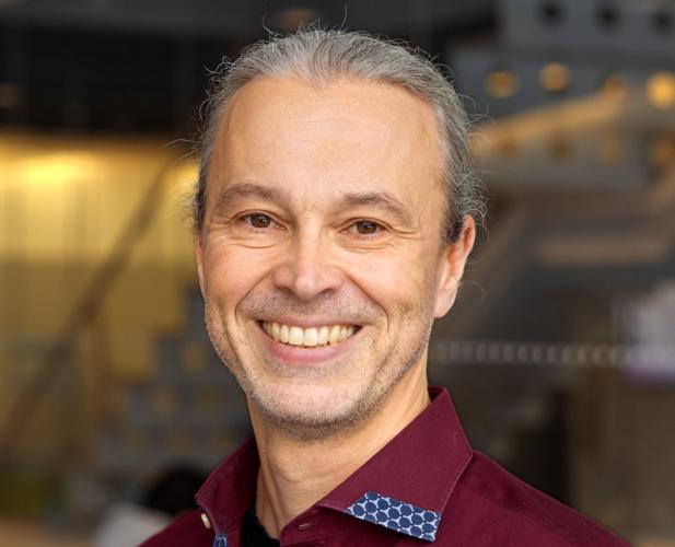 A portrait of Thorsten Joachims, a man with gray hair and a dark red shirt smiling at the camera