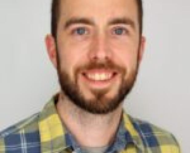 a man with short brown hair and a beard wearing a yellow and blue plaid shirt