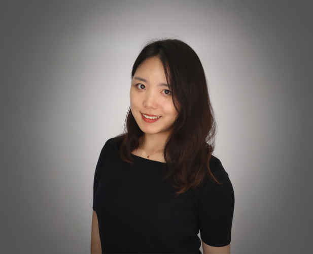 A color photo of woman in a black dress in front of a grey background.