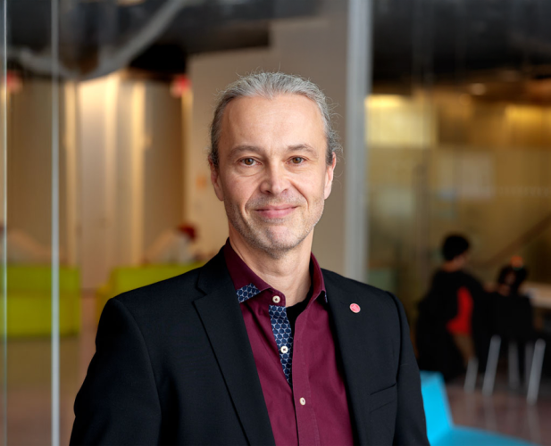 A portrait of Thorsten Joachims, a man with gray hair and a dark red shirt smiling at the camera