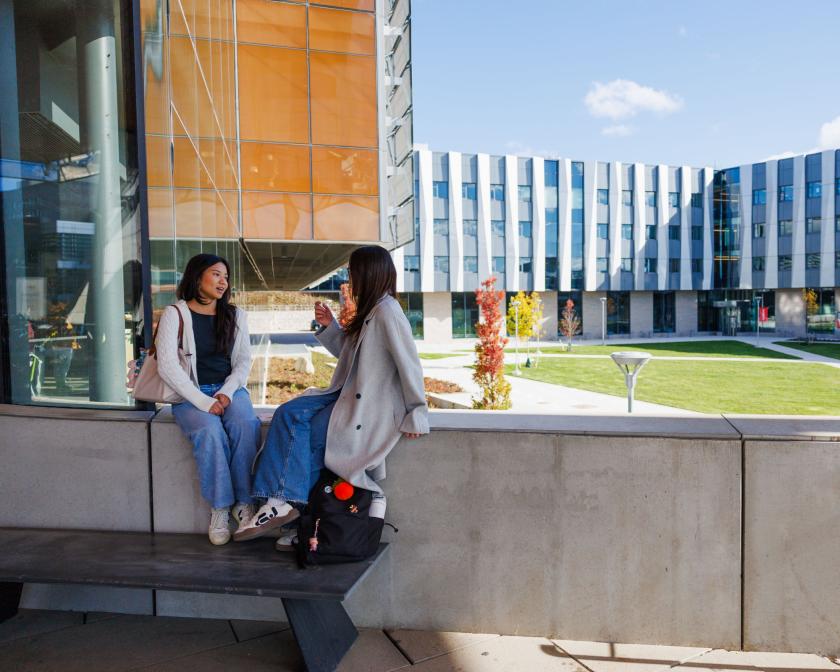 two female students sit on a ledge