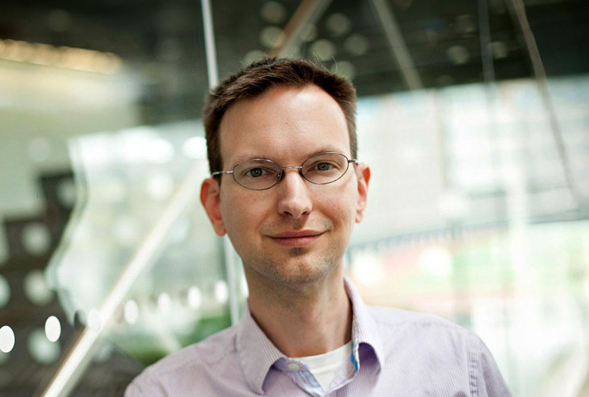 Portrait of David Mimno standing indoors near a glass wall.