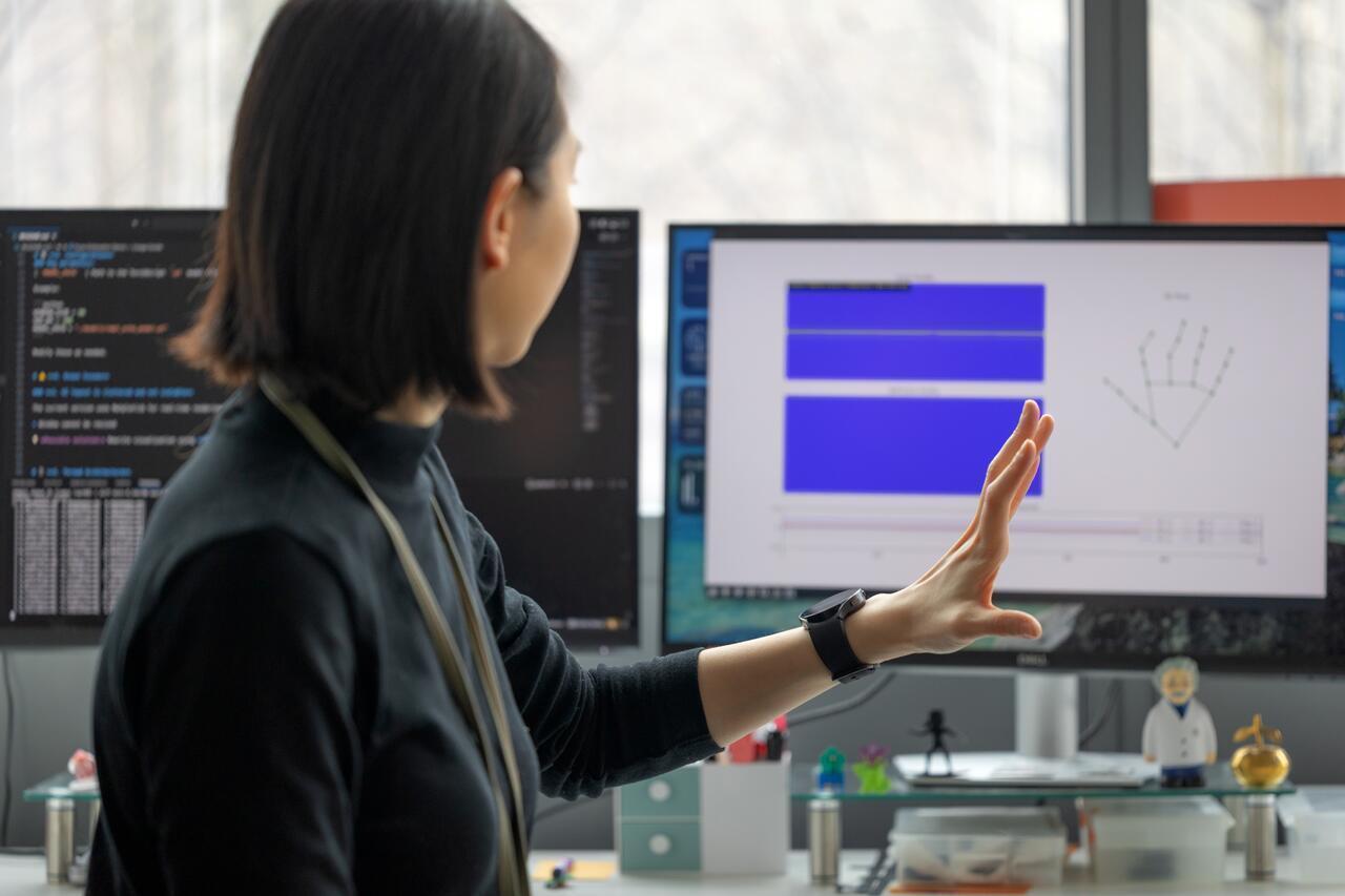 a women with short black hair holds up a hand in front of a computer screen